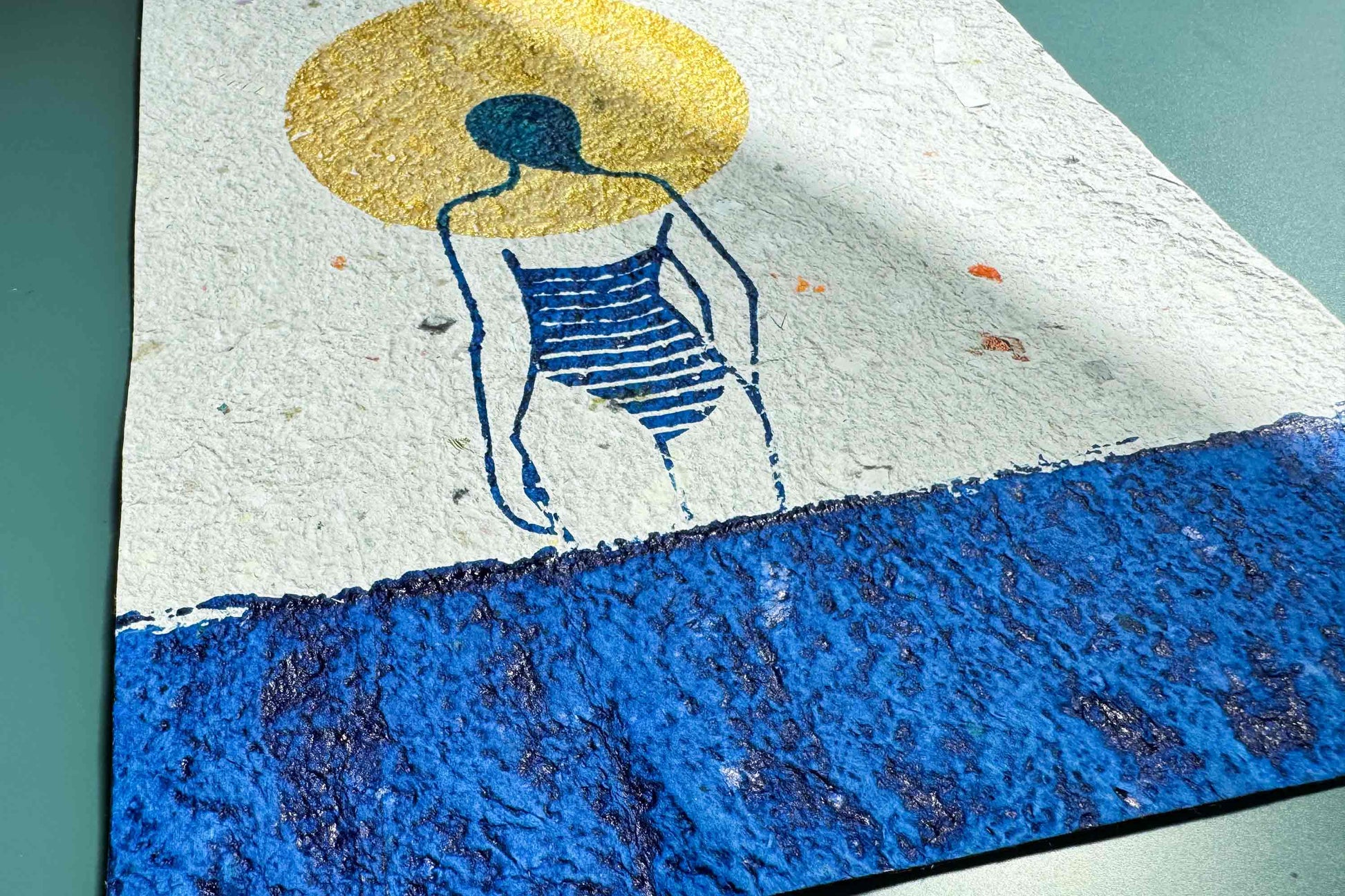 Close up Siebdruckplakat Mare vor blauem Hintergrund: schimmerndene goldene Sonne, blaues Wasser und Silhouette die in die Ferne guckt. Handbedruckt auf selbst geschöptem, strukturiertem Papier, Upcycling Altpapier