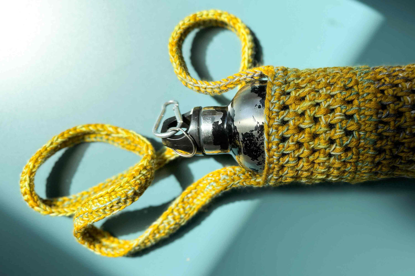 Detailansicht eines gelben gehäkelten Flaschenhalters zum Umhängen für Wanderungen oder Festivals aus geretteter Wolle