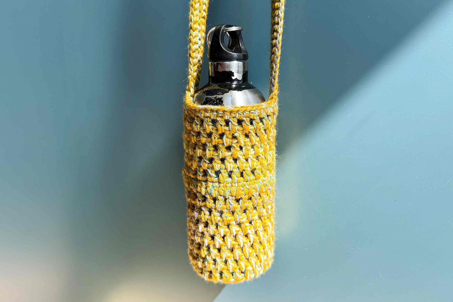 Hängender gelber gehäkelter Flaschenhalter zum Umhängen als Festivalgadget aus geretteter Wolle