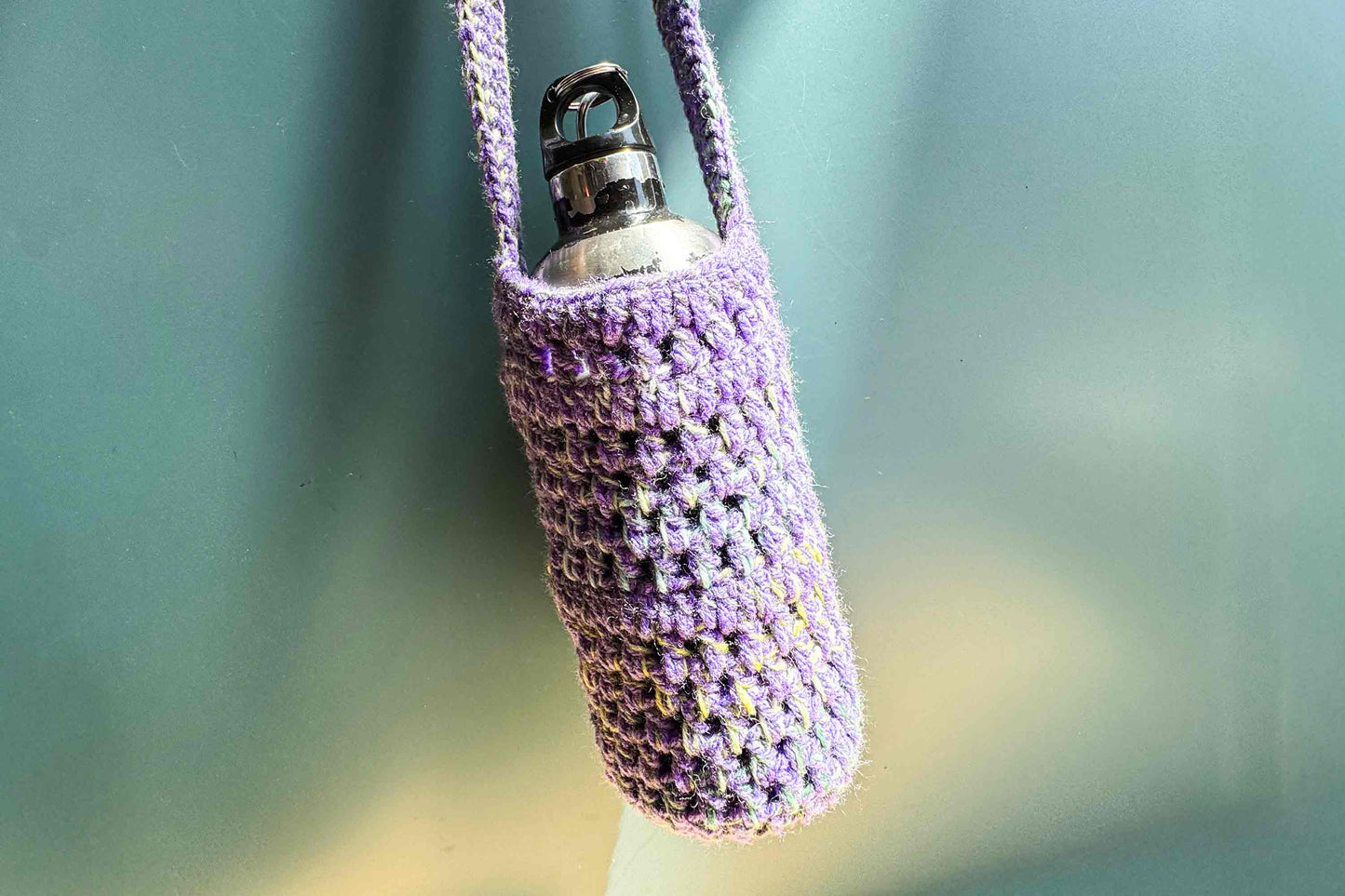 Hängender, gehäkelter Flaschenhalter in lila bunt gemixter Wolle