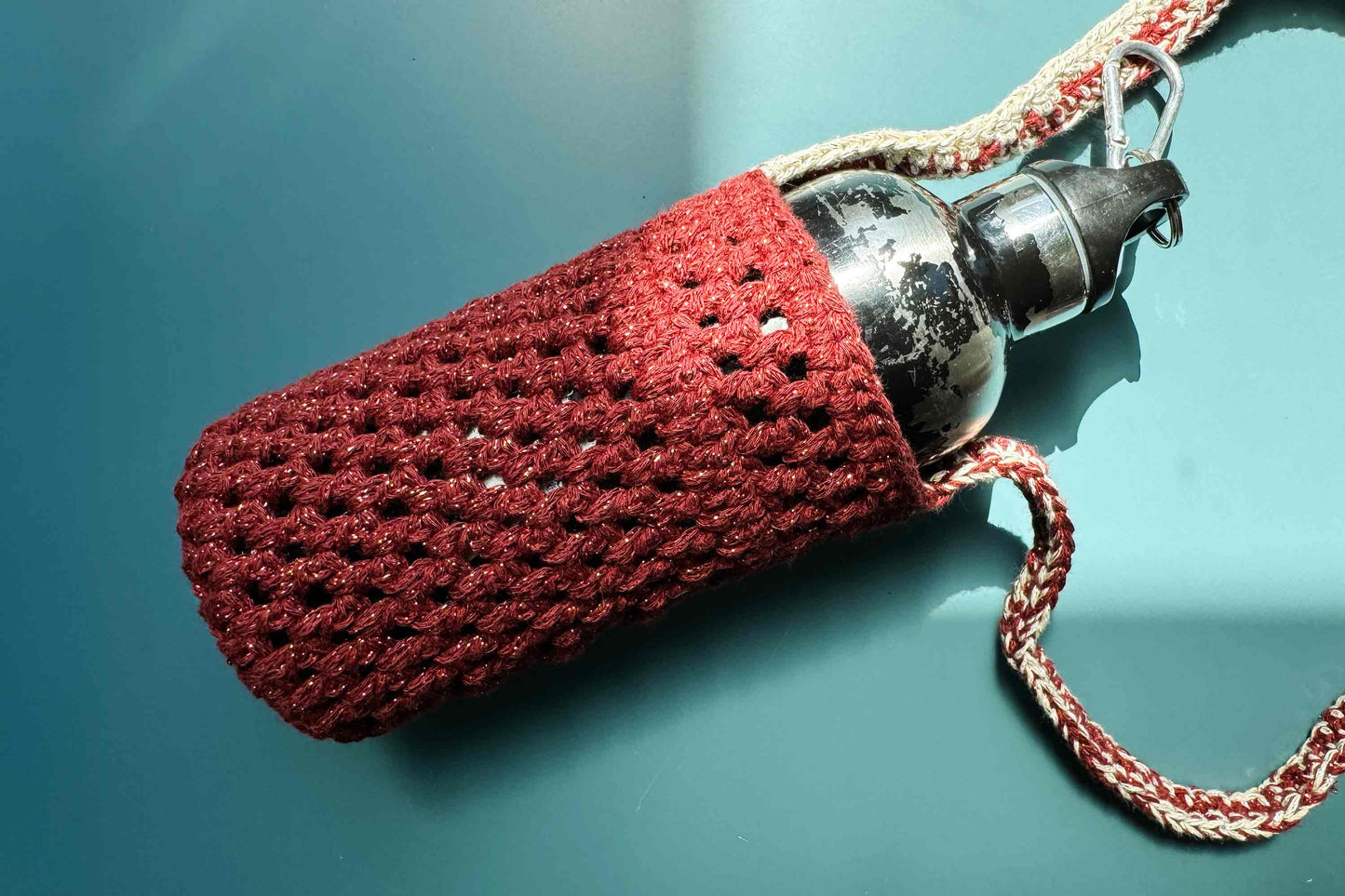 Detailansicht des gehäkelten, rot-beige glitzernden Flaschenhalters zum Umhängen CHRISTA mit Trinkflasche