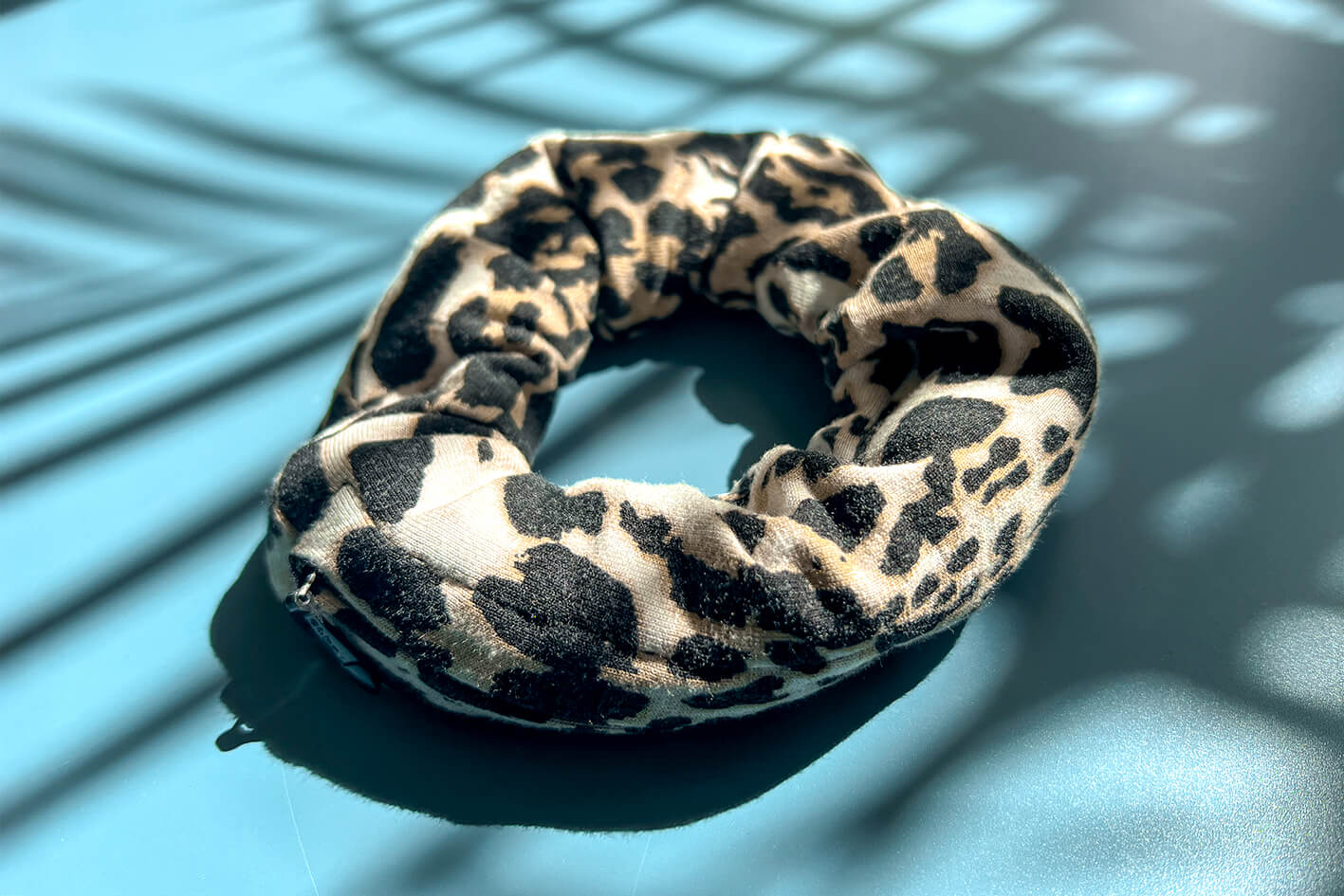 Ein Scrunchie mit Reißverschluss und klassichem braun-weiß-grauem Leopardenmuster liegt auf einem blauen Tisch. Der Reißverschluss ist geöffnet.