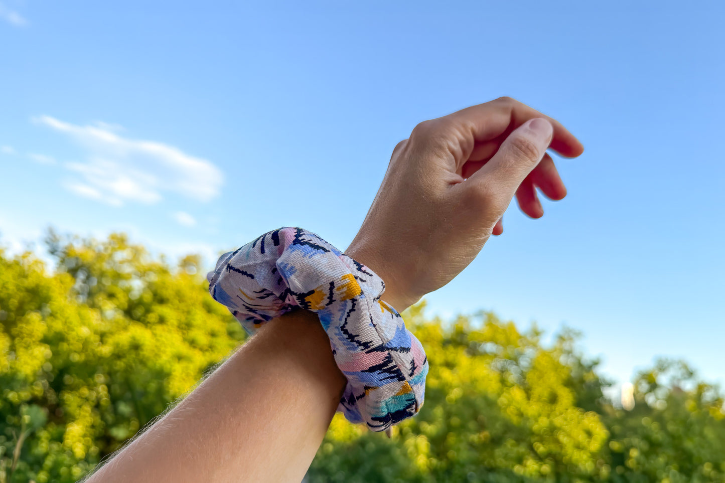 Eine Frauenhand trägt einen beigen Scrunchie mit buntem Muster und Reißverschluss. Der Reißverschluss ist geschlossen. Jeff - EveryPieceAFriend