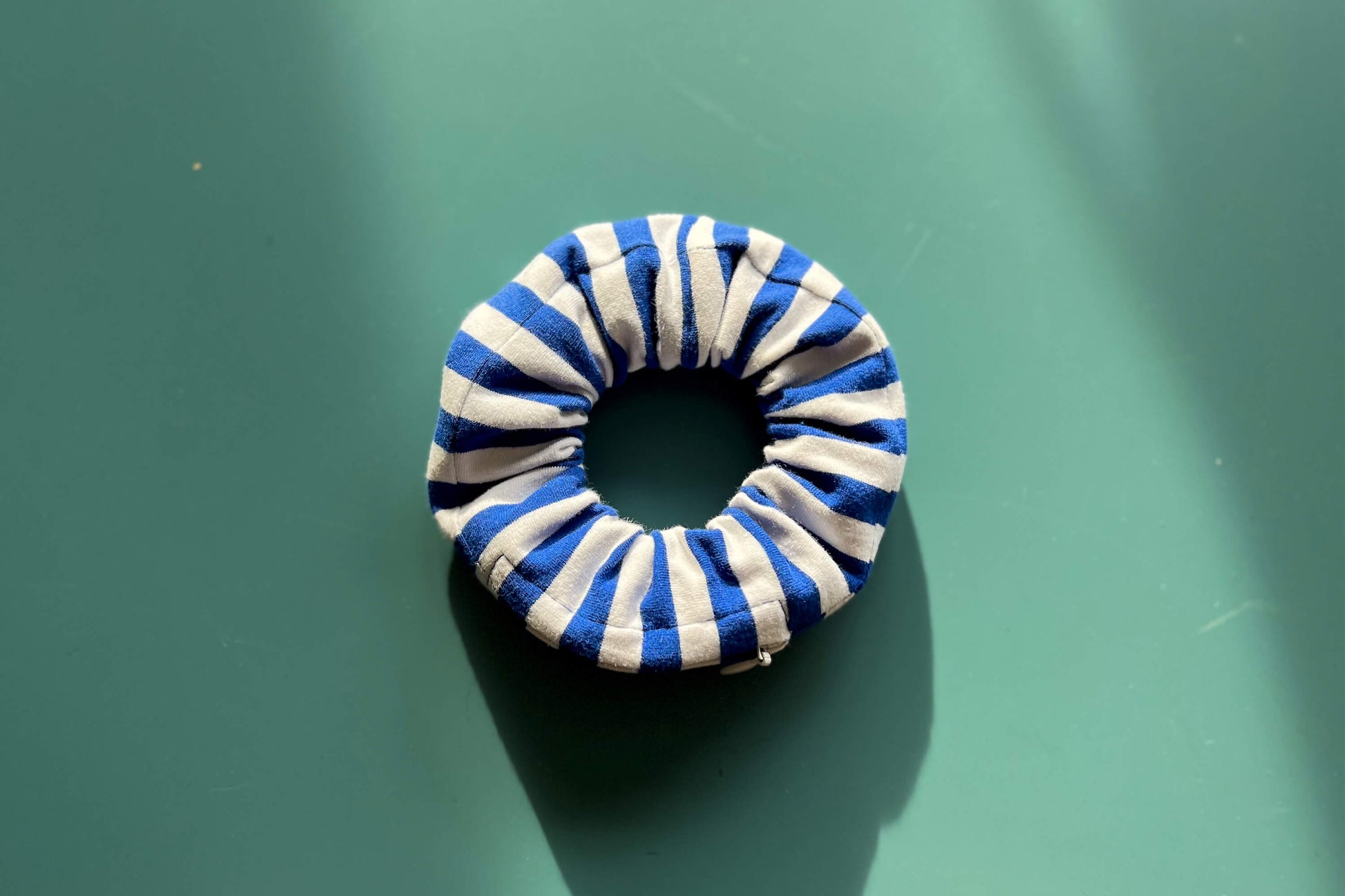 Anischt von oben: Ein Scrunchie mit Reißverschluss und einem Muster in hellblau und weiß liegt auf einem blauen Tisch. Der Reißverschluss ist geschlossen und hat die Farbe weiß.
