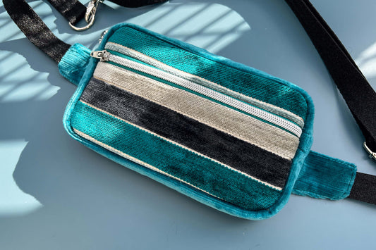 Gesamtansicht einer Bauchtasche aus Samt von Jeff EveryPieceAFriend. Die Tasche ist blau und grau gestreift, hat ein schwarzes Gurtband und einen silbernen Reißverschluss.
