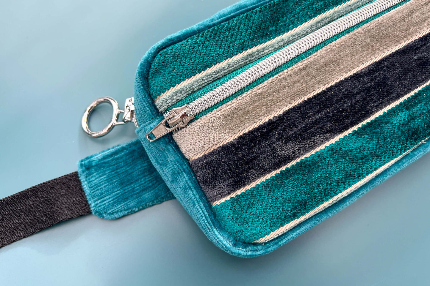 Detailansicht einer Bauchtasche aus Samt von Jeff EveryPieceAFriend. Die Tasche ist blau und grau gestreift, hat ein schwarzes Gurtband und einen silbernen Reißverschluss.