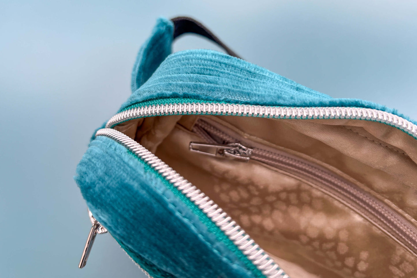 Detailansicht einer geöffneten Bauchtasche aus Samt von Jeff EveryPieceAFriend. Die Tasche ist blau und hat ein schwarzes Gurtband und einen silbernen Reißverschluss. Das Innenfach der Tasche ist gold und zeigt ein extra Fach mit Reißverschluss.