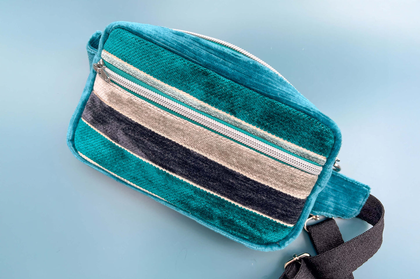 Gesamtansicht einer Bauchtasche aus Samt von Jeff EveryPieceAFriend. Die Tasche ist blau und grau gestreift, hat ein schwarzes Gurtband und einen silbernen Reißverschluss.