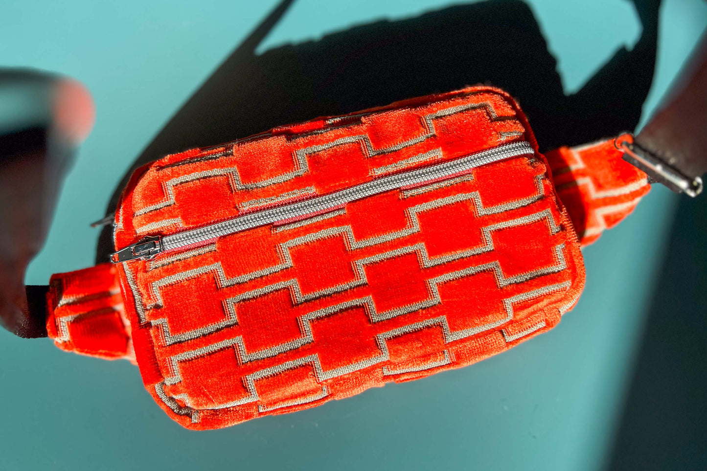 Gesamtansicht einer Bauchtasche aus upcycled Möbelstoff von Jeff EveryPieceAFriend. Die Tasche ist orange gemustert, hat ein schwarzes Gurtband und einen silbernen Reißverschluss.