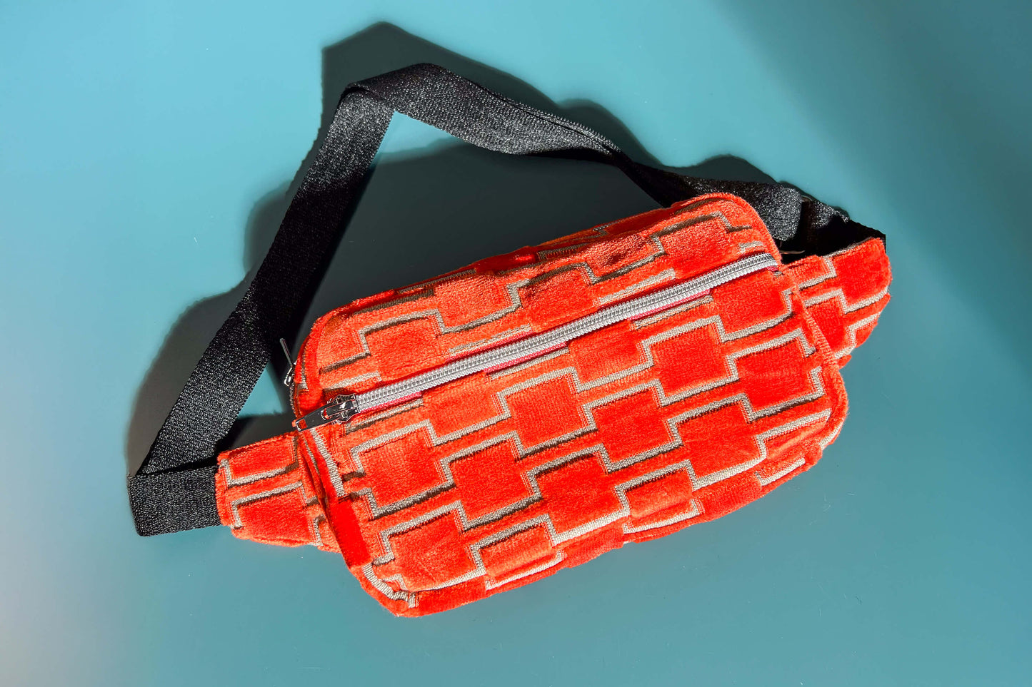 Gesamtansicht einer Bauchtasche aus upcycled Möbelstoff von Jeff EveryPieceAFriend. Die Tasche ist orange gemustert, hat ein schwarzes Gurtband und einen silbernen Reißverschluss.