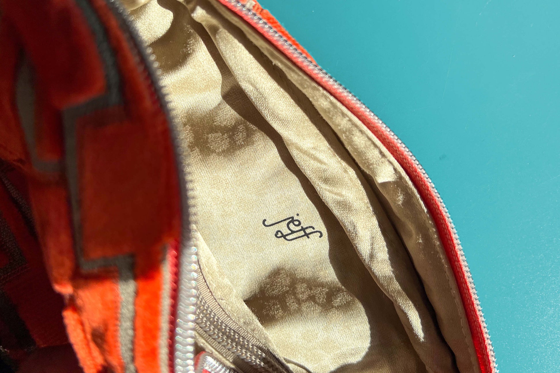 Detailansicht einer geöffneten Bauchtasche aus upcycled Möbelstoff von Jeff EveryPieceAFriend. Die Tasche ist orange gemustert, hat ein schwarzes Gurtband und einen silbernen Reißverschluss. Das Innenfach der Tasche ist beige.