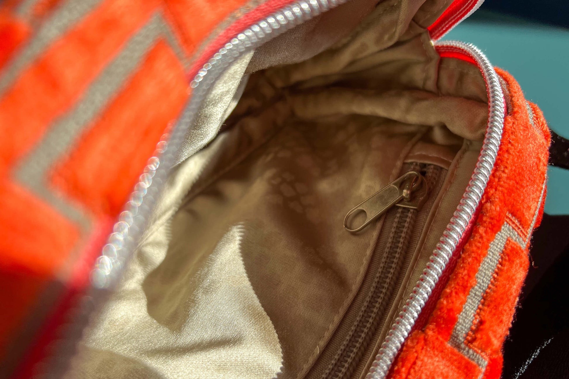 Detailansicht einer geöffneten Bauchtasche aus upcycled Möbelstoff von Jeff EveryPieceAFriend. Die Tasche ist orange gemustert, hat ein schwarzes Gurtband und einen silbernen Reißverschluss. Das Innenfach der Tasche ist beige.