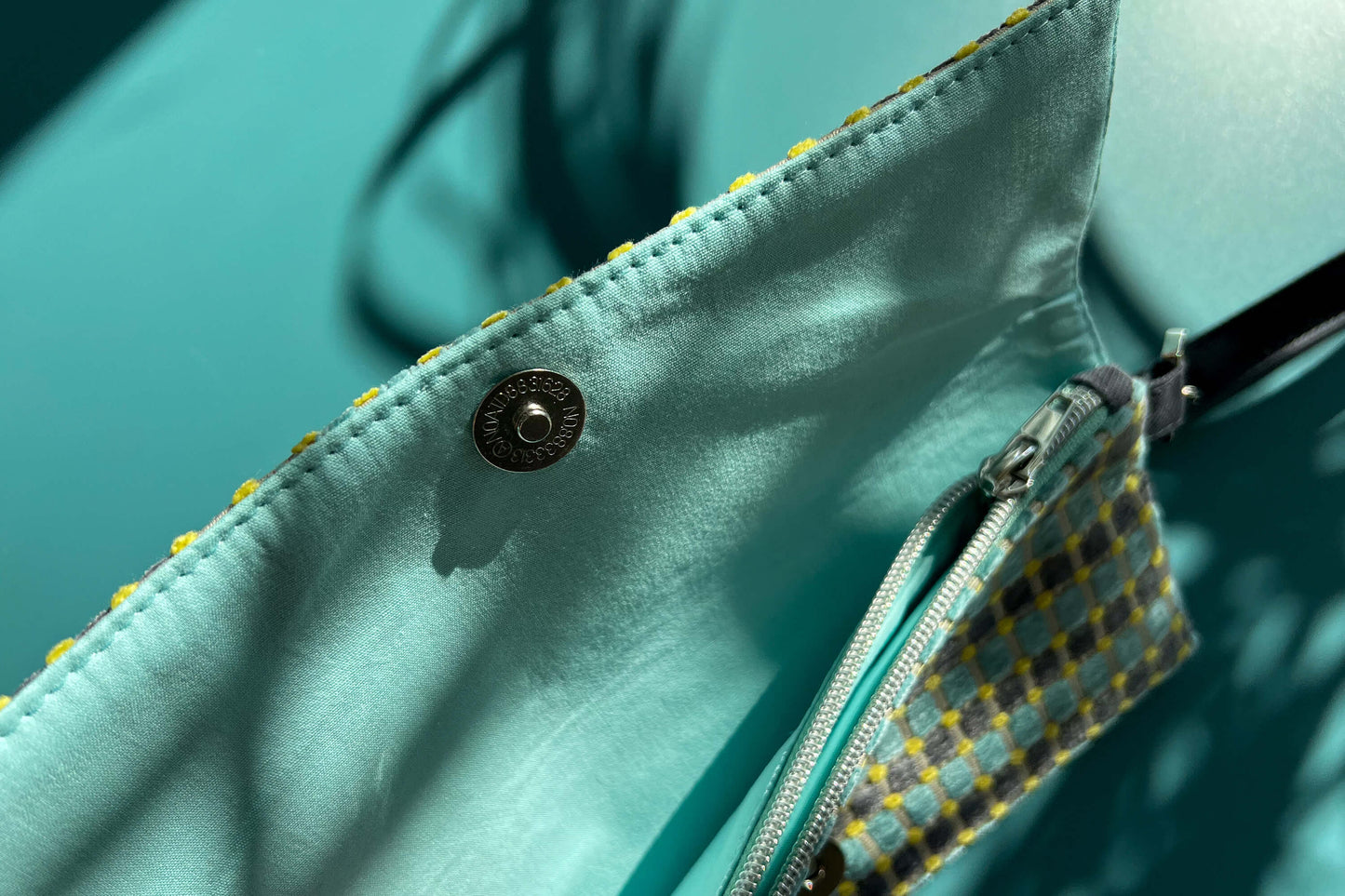 Detailansicht der geöffneten, kleinen Umhängetasche DANA aus upcycled Polsterstoff in den Farben blau, gelb und beige mit silbernen Verschlüssen.