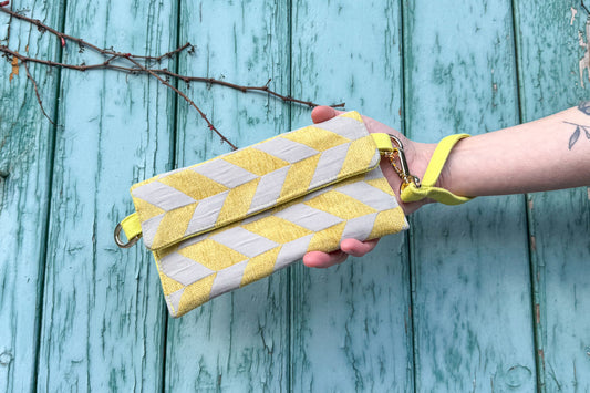Gesamtansicht: Hand hält Umhängetasche DANA aus upcycled gold-silbernen Polsterstoff vor blauem Hintergrund ins Bild.