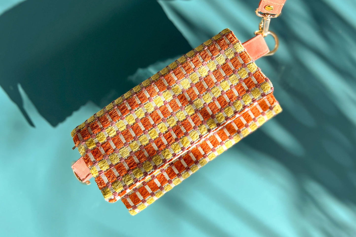 Gesamtansicht der Handtasche DANA in der Farbe gelb-orange-beige. Die Tasche liegt auf einem blauen Untergrund.