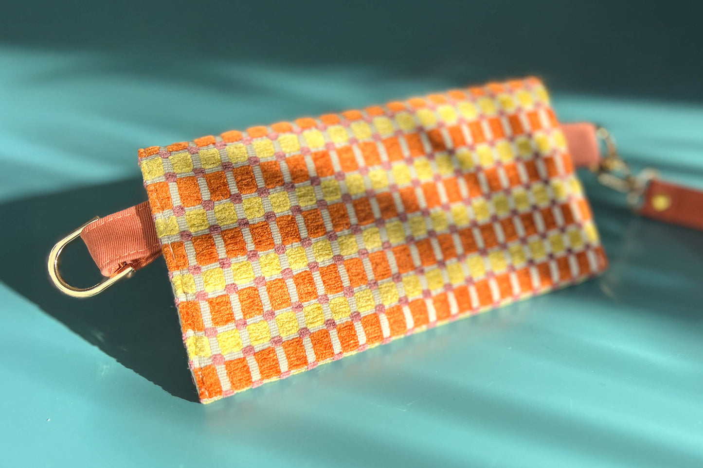 Gesamtansicht der Rücseite der Handtasche DANA in der Farbe gelb-orange-beige. Die Tasche liegt auf einem blauen Untergrund.