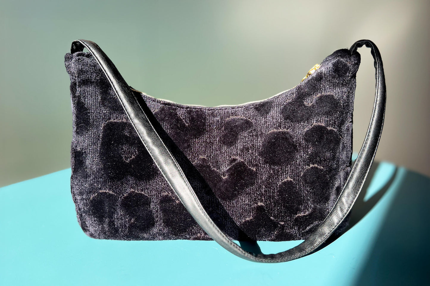 Gesamtansicht: Schultertasche im Vintagestil vor blau-grauem Hintergrund. Die Tasche ist schwarz gemustert und aus Samt. Die Tasche wurde aus upcycled Materialien von Jeff Every Piece A Friend hergestellt