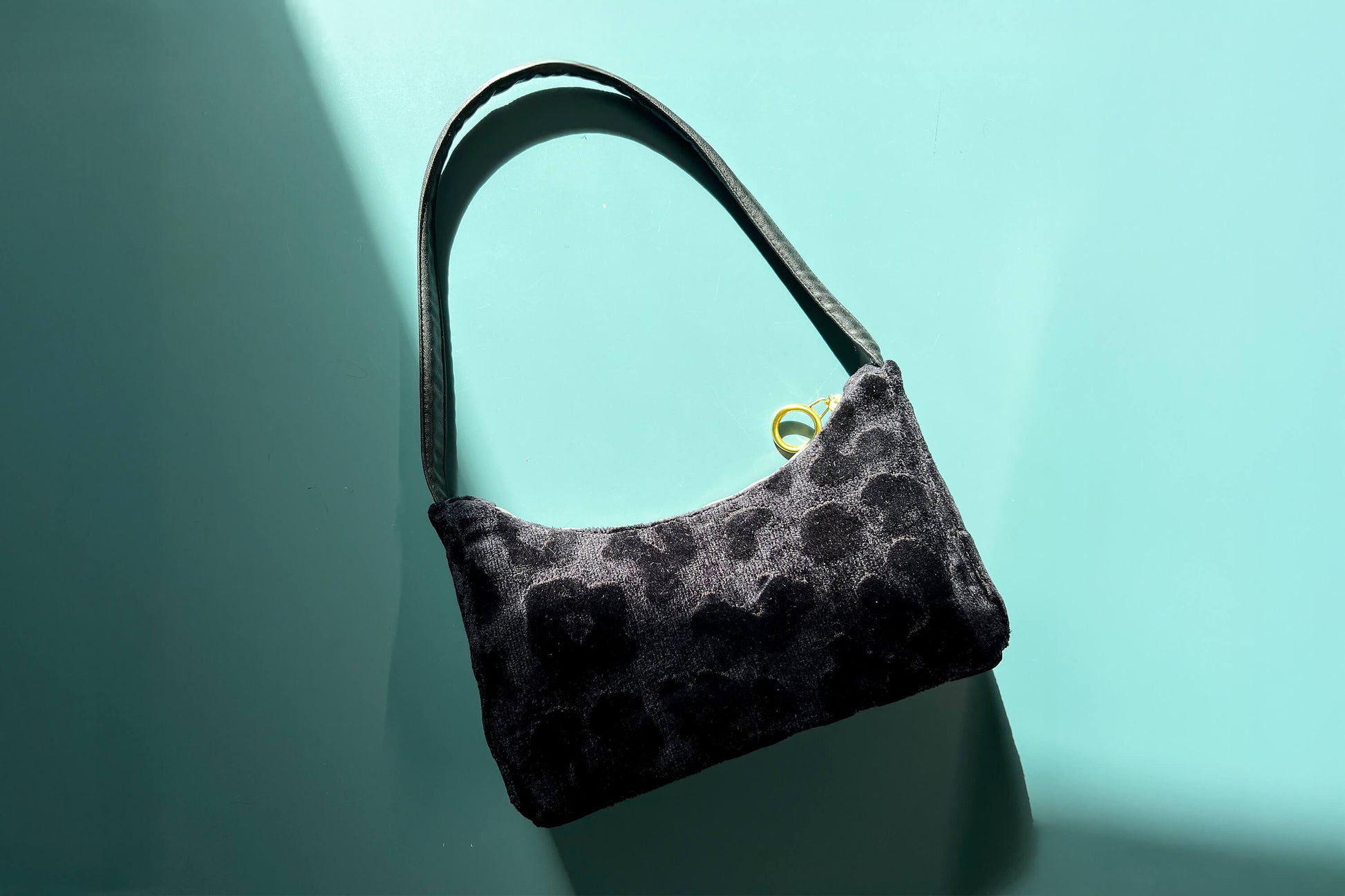 Gesamtansicht: Schultertasche im Vintagestil vor blau-grauem Hintergrund. Die Tasche ist schwarz gemustert und aus Samt. Die Tasche wurde aus upcycled Materialien von Jeff Every Piece A Friend hergestellt