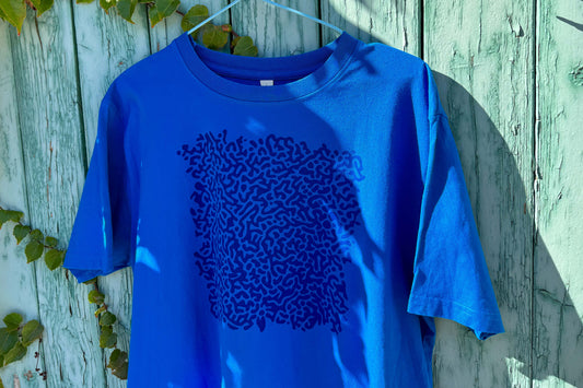 Detailansicht von einem blauen T-Shirt vor einem blauen Hintergrund. Das T-Shirt hat einen welligen Druck auf der Brust.