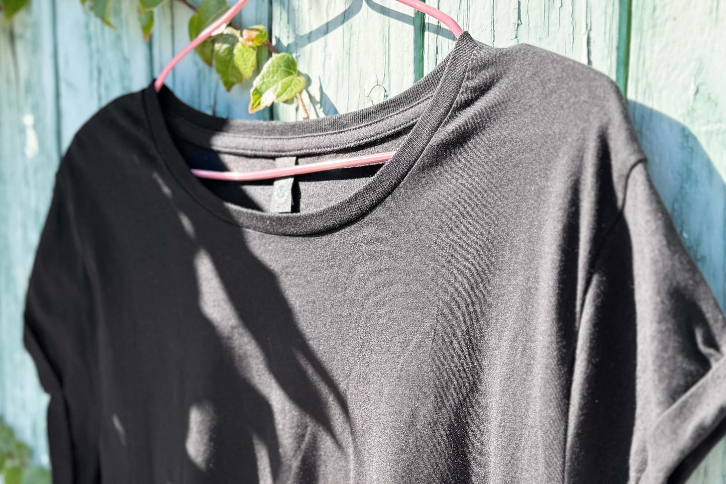 Vordere Detailansicht von einem schwarzen T-Shirt vor einem blauen Hintergrund.