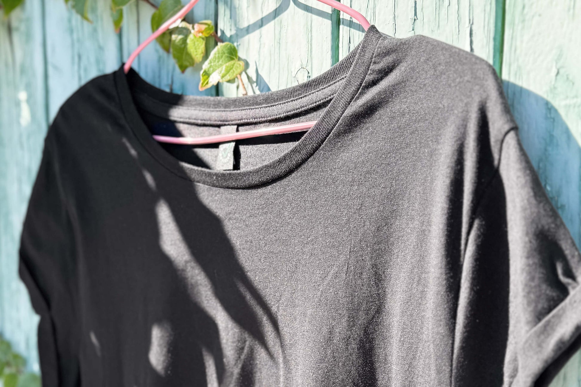 Vordere Detailansicht von einem schwarzen T-Shirt vor einem blauen Hintergrund.