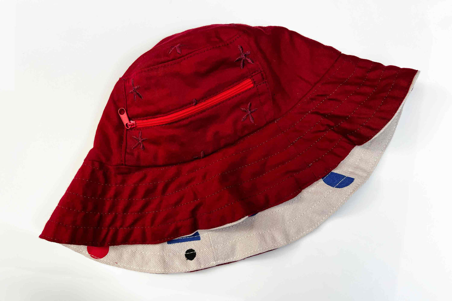Wendbarer Sommerhut aus Upycling-materialien: eine Seite rot mit kleinem Reisverschlussfach, die andere Seite veredelt mit händischem Siebdruck aus bunten geometrischen Formen