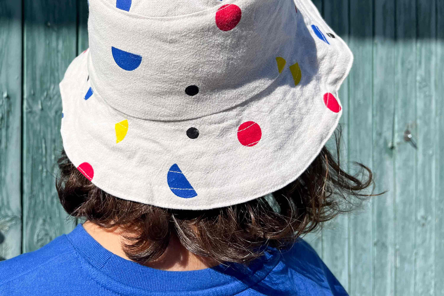 Frau trägt wendbaren Sommerhut LUCA aus Upycling-materialien. Der Hut ist veredelt mit händischem Siebdruck aus bunten geometrischen Formen