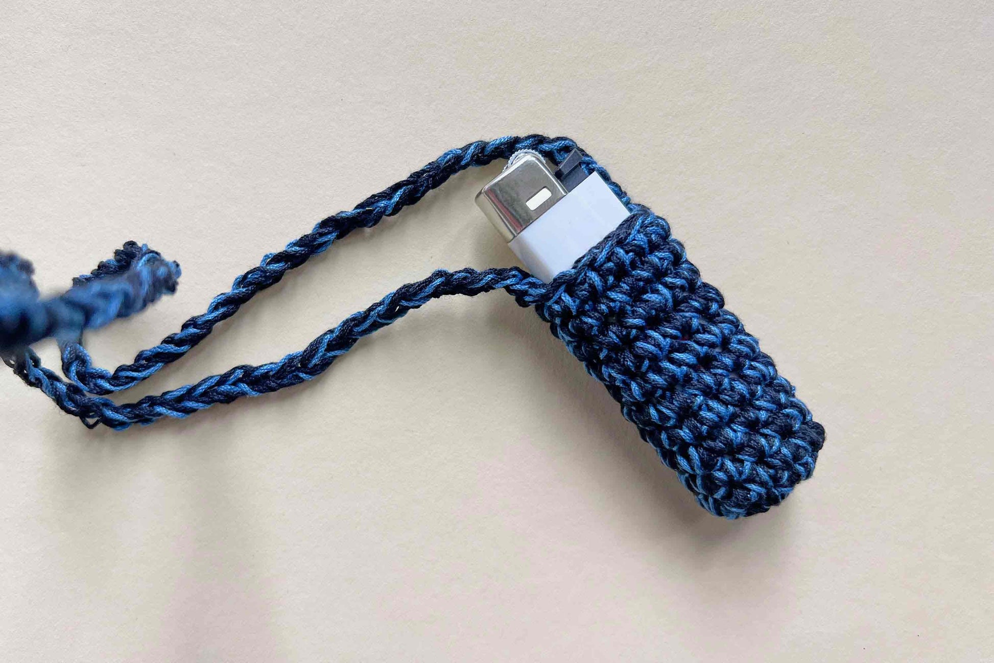 Gehäkelter blauer Feuerzeughalter auf hellem Hintergrund