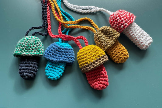 Fünf bunte und gehäkelte Feuerzeughalter oder Lippenstifttaschen als Festivalaccessoire liegen in verschiedenen Farben auf blauem Hintergrund.