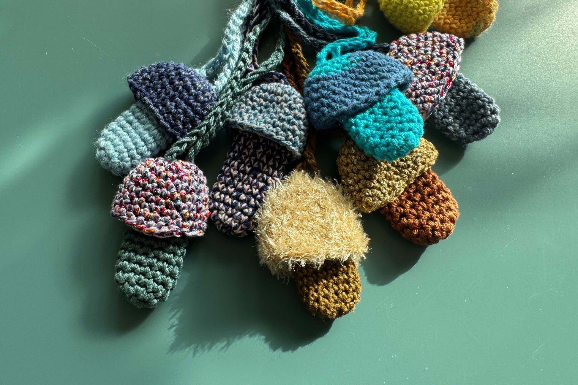 Mehrere gehäkelte Feuerzeughalter oder Lippenstifttaschen als Festivalaccessoire liegen auf blauem Hintergrund.