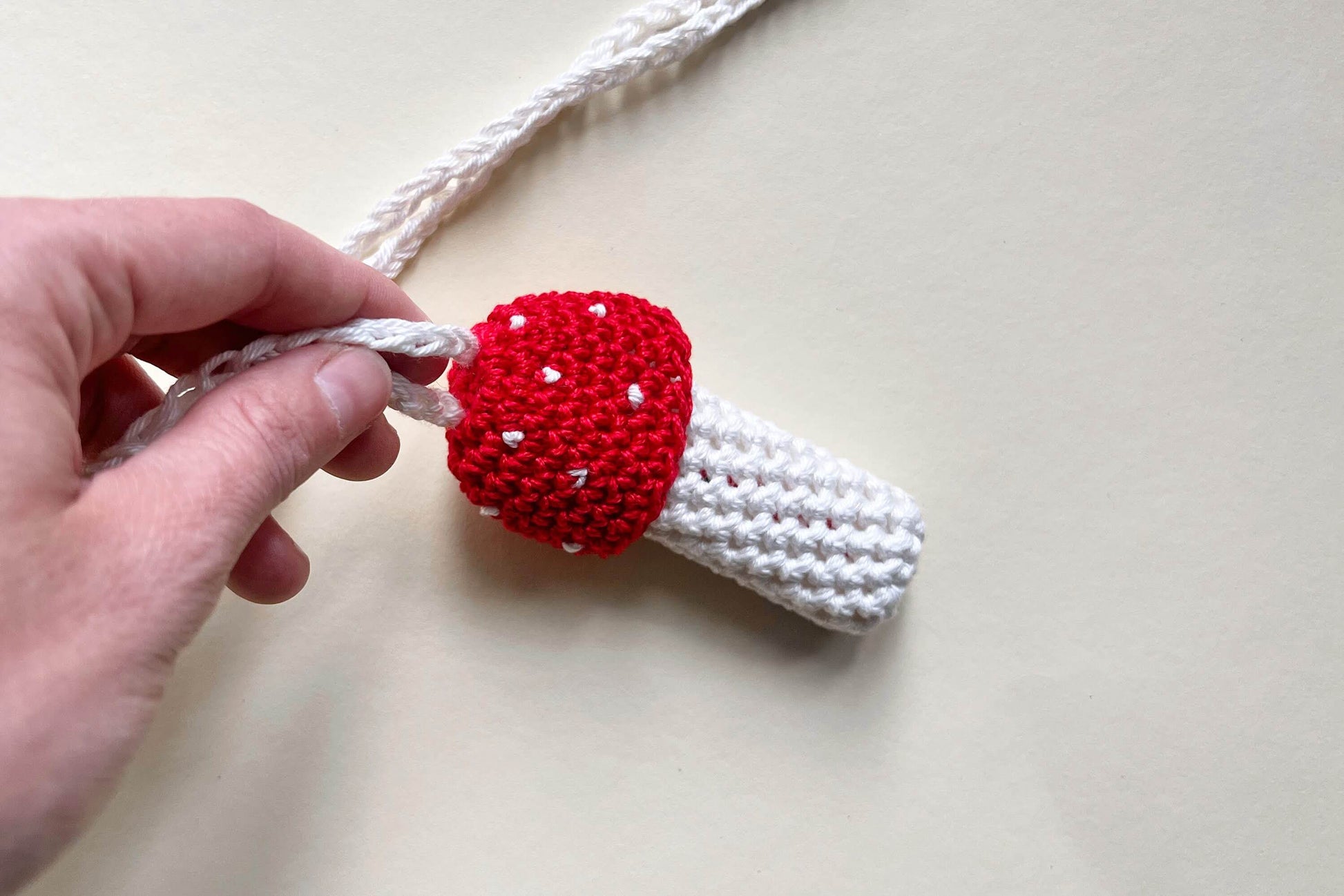 Hand hält einen gehäkelten Feuerzeughalter zum Umhängen in Fliegenpilzoptik