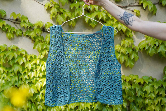 Gehäkelte türkise Strickweste VANYA ins Bild gehlante von einer Frauenhand vor einem Hintergrund aus Efeu