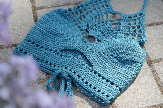 Detailansicht des gehäkelten Tops PINA in metallic blau vor grauem Hintergrund.