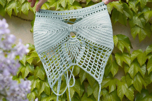 Zwei Hände halten das gehäkelte Top PINA in die Kamera in der Farbe mint vor einem Hintergrund aus Efeu.