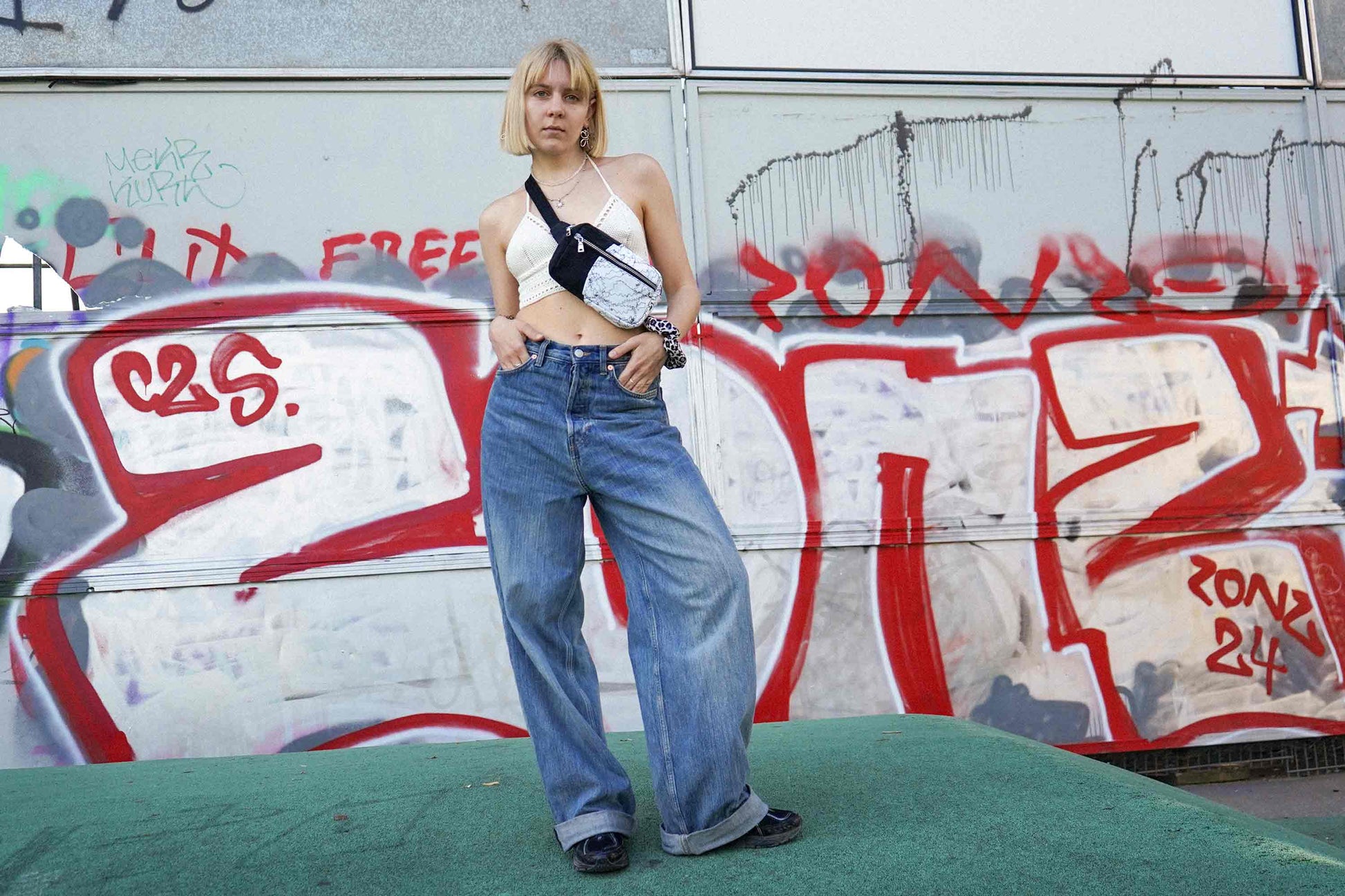 Junge Frau steht vor Graffiti-Wand und trägt Hipbag PAOLINA aus upgecyelten Materialien von jeff every piece a friend