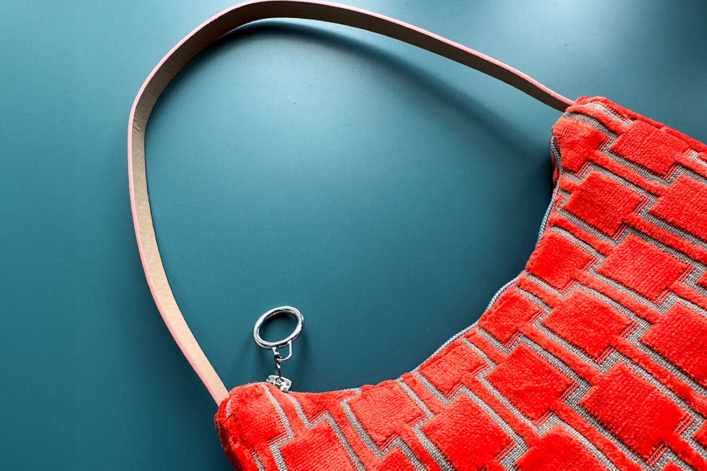 Detailansicht: Schultertasche im Vintagestil vor blauen Hintergrund. Die Tasche ist orange gemustert und aus Samt und hat einen silbernen Reißverschluss. Die Tasche wurde aus upcycled Materialien von Jeff Every Piece A Friend hergestellt.