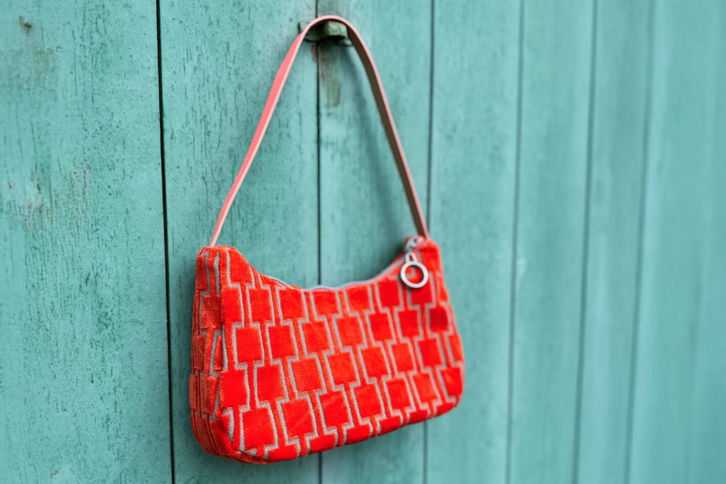 Gesamtansicht: Schultertasche im Vintagestil vor blauen Hintergrund. Die Tasche ist orange gemustert und aus Samt. Die Tasche wurde aus upcycled Materialien von Jeff Every Piece A Friend hergestellt.