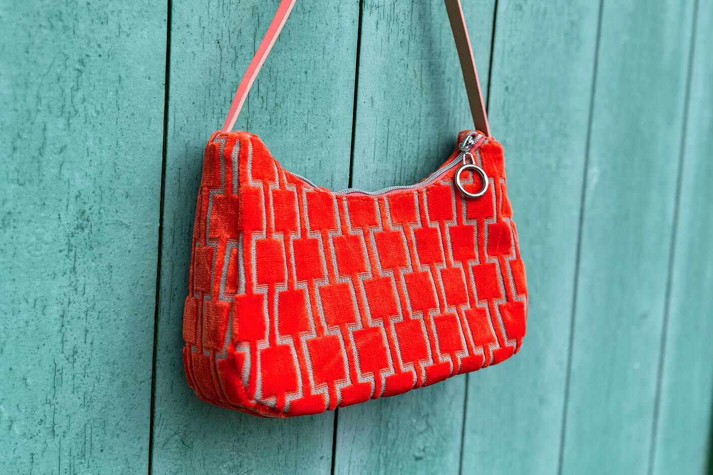 Gesamtansicht: Schultertasche im Vintagestil vor blauen Hintergrund. Die Tasche ist orange gemustert und aus Samt. Die Tasche wurde aus upcycled Materialien von Jeff Every Piece A Friend hergestellt.