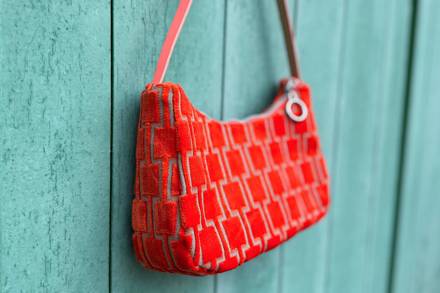 Seitliche Gesamtansicht: Schultertasche im Vintagestil vor blauen Hintergrund. Die Tasche ist orange gemustert und aus Samt. Die Tasche wurde aus upcycled Materialien von Jeff Every Piece A Friend hergestellt.