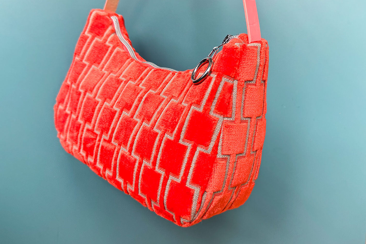 Seitliche Detailansicht: Schultertasche im Vintagestil vor blauen Hintergrund. Die Tasche ist orange gemustert und aus Samt. Die Tasche wurde aus upcycled Materialien von Jeff Every Piece A Friend hergestellt.