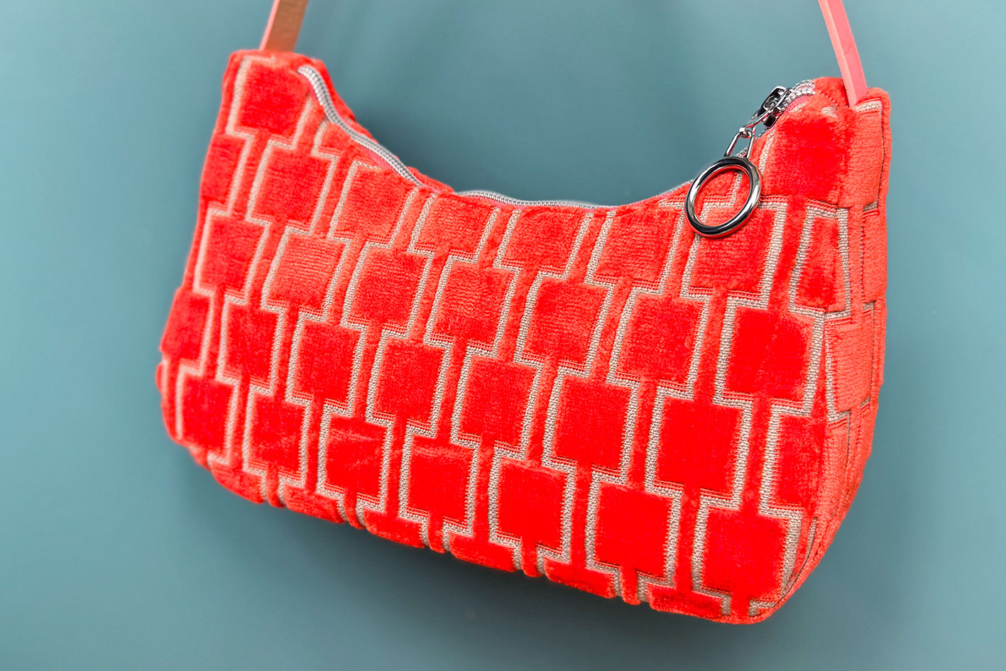 Detailansicht: Schultertasche im Vintagestil vor blauen Hintergrund. Die Tasche ist orange gemustert und aus Samt. Die Tasche wurde aus upcycled Materialien von Jeff Every Piece A Friend hergestellt.