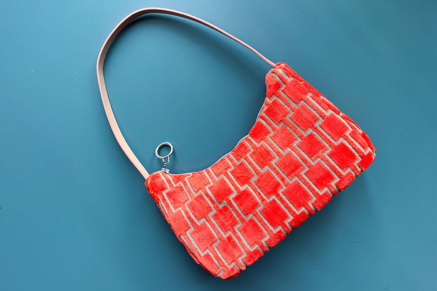 Gesamtansicht: Schultertasche im Vintagestil vor blauen Hintergrund. Die Tasche ist orange gemustert und aus Samt. Die Tasche wurde aus upcycled Materialien von Jeff Every Piece A Friend hergestellt.