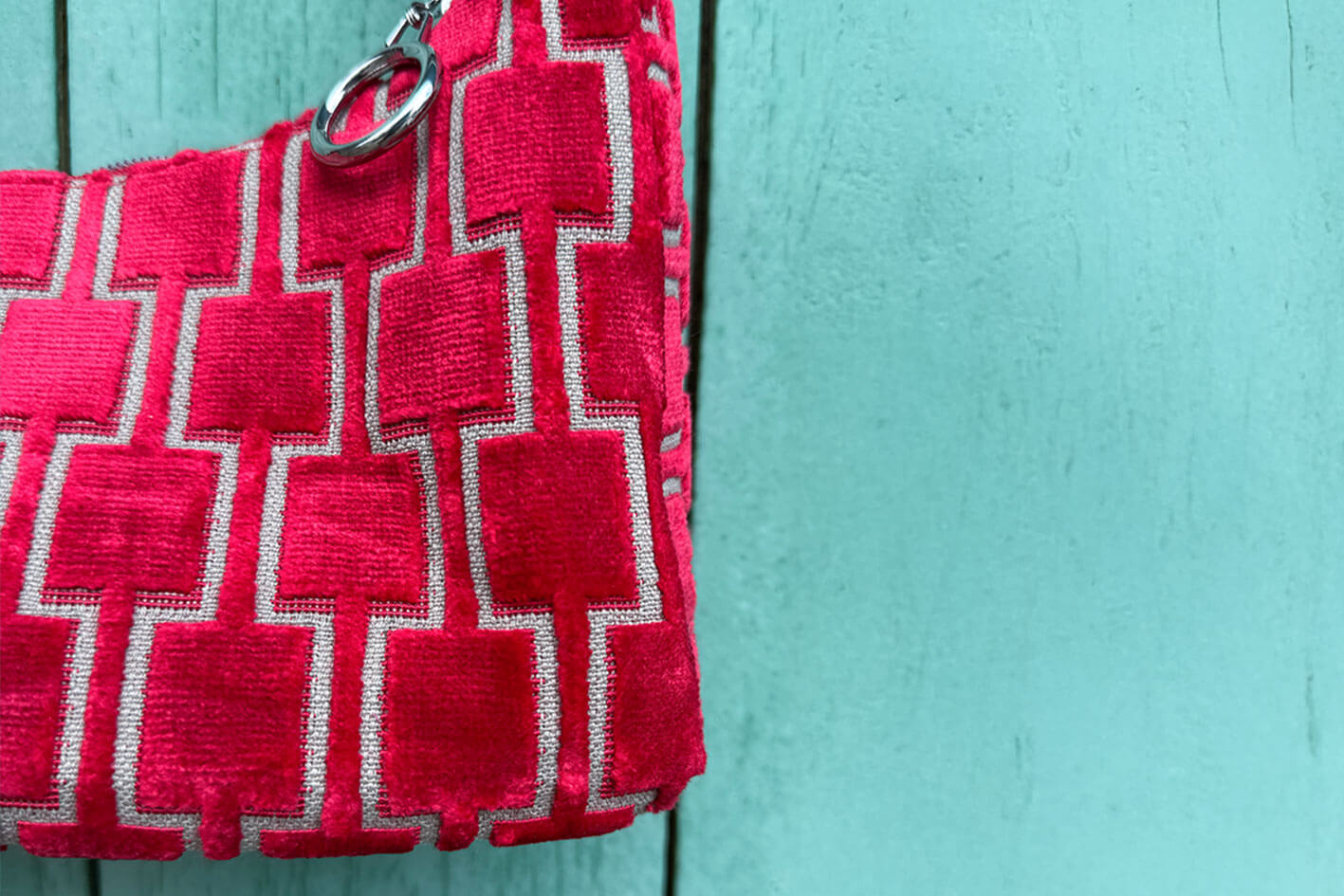 Detailansicht: Schultertasche im Vintagestil vor blauen Hintergrund. Die Tasche ist rot gemustert und aus Samt und hat einen silbernen Reißverschluss. Die Tasche wurde aus upcycled Materialien von Jeff Every Piece A Friend hergestellt.