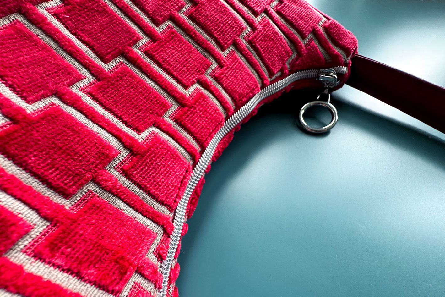 Detailansicht: Schultertasche im Vintagestil vor blauen Hintergrund. Die Tasche ist rot gemustert und aus Samt und hat einen silbernen Reißverschluss. Die Tasche wurde aus upcycled Materialien von Jeff Every Piece A Friend hergestellt.