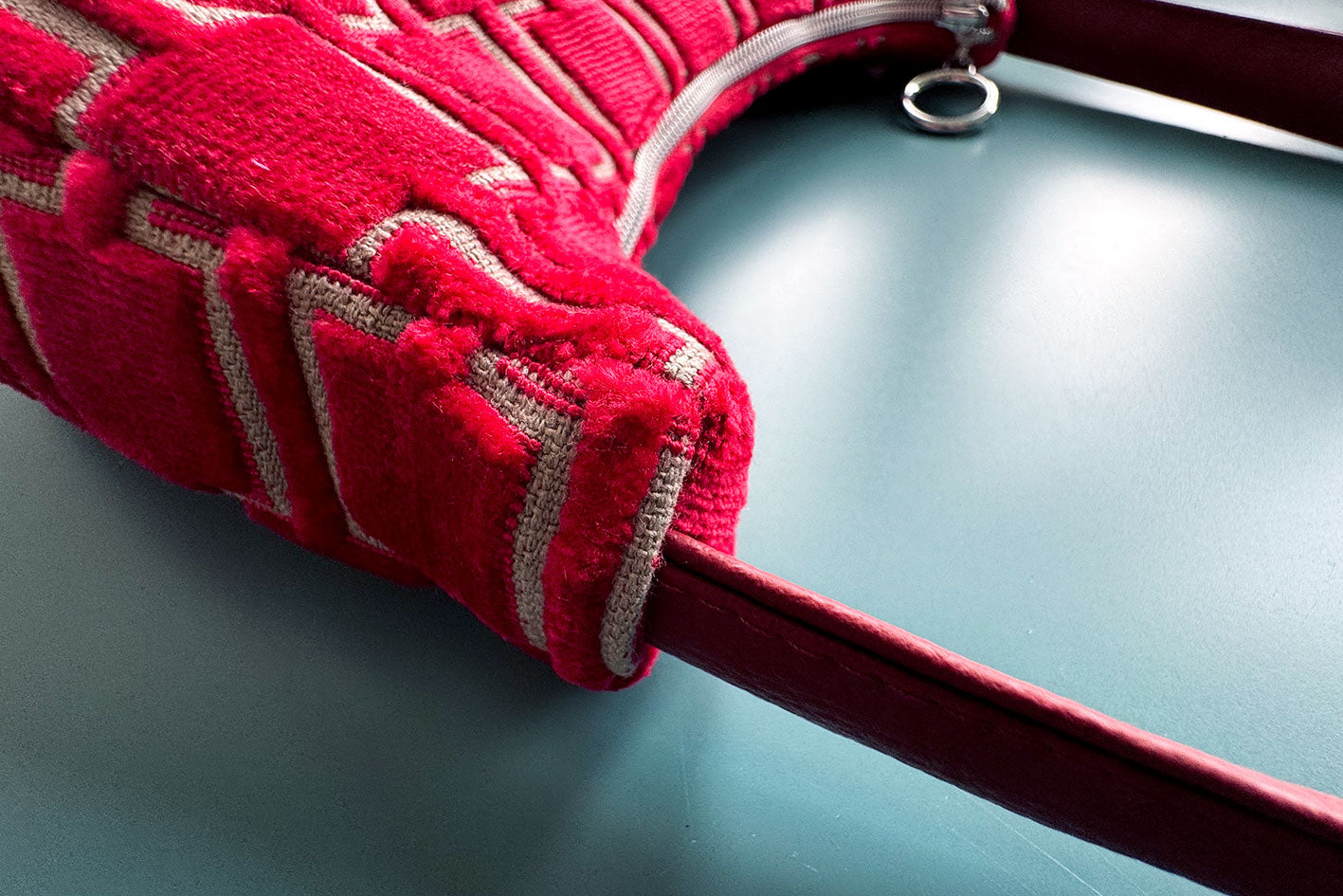 Detailansicht: Schultertasche im Vintagestil vor blauen Hintergrund. Die Tasche ist rot gemustert und aus Samt und hat einen silbernen Reißverschluss. Die Tasche wurde aus upcycled Materialien von Jeff Every Piece A Friend hergestellt.