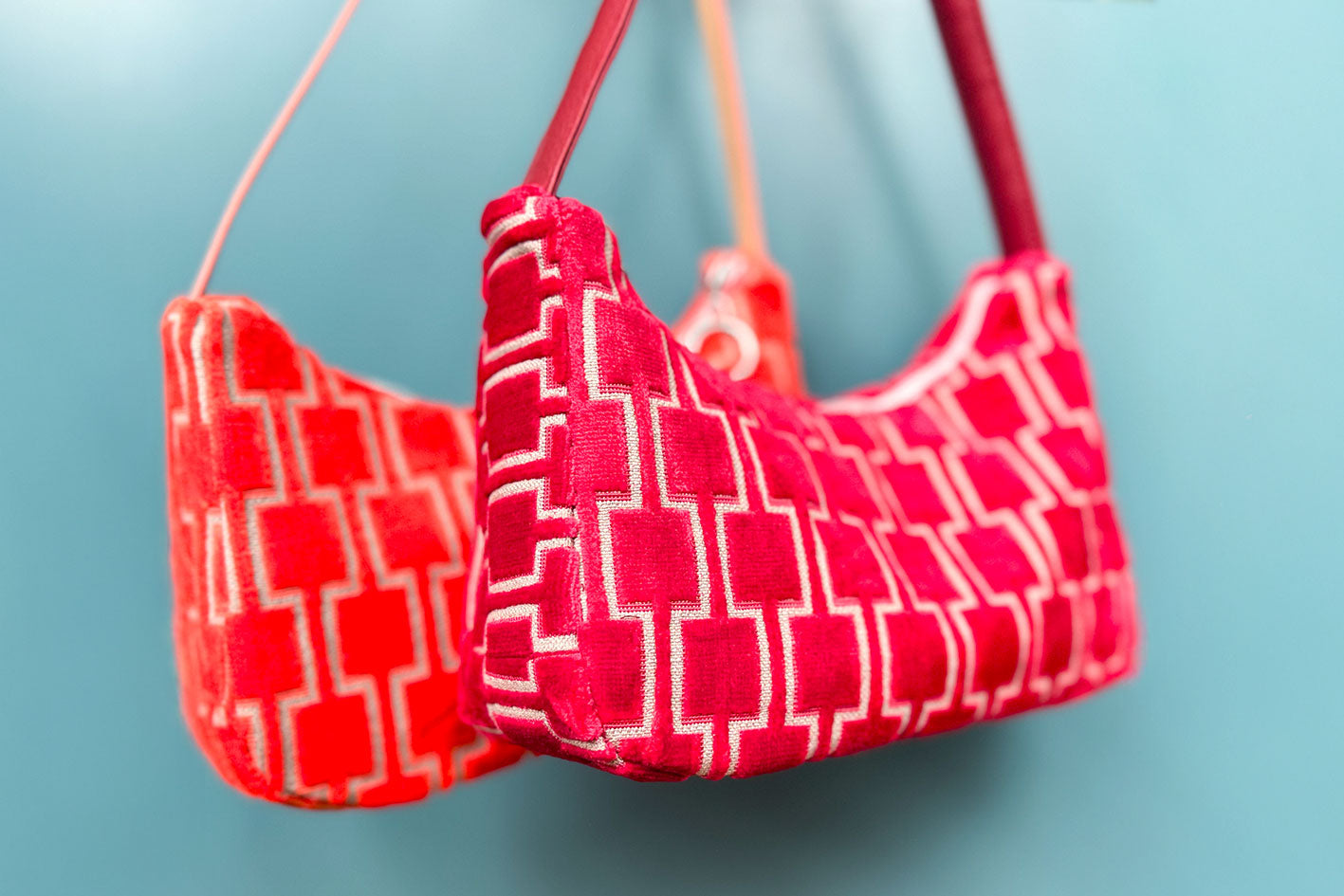 Gesamtansicht: Zwei Schultertaschen im Vintagestil vor blauen Hintergrund. Vordere Tasche ist rot gemustert, die hintere Tasche ist orange gemustert. Beide Taschen wurden von aus upcycled Materialien von Jeff Every Piece A Friend hergestellt.