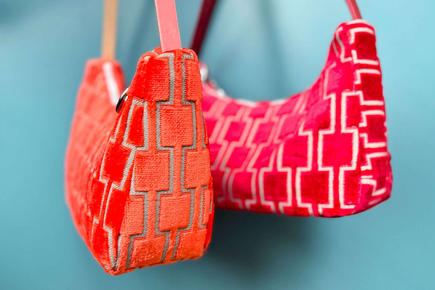 Gesamtansicht: Zwei Schultertaschen im Vintagestil vor blauen Hintergrund. Vordere Tasche ist orange gemustert, die hintere Tasche ist rot gemustert. Beide Taschen wurden von aus upcycled Materialien von Jeff Every Piece A Friend hergestellt.