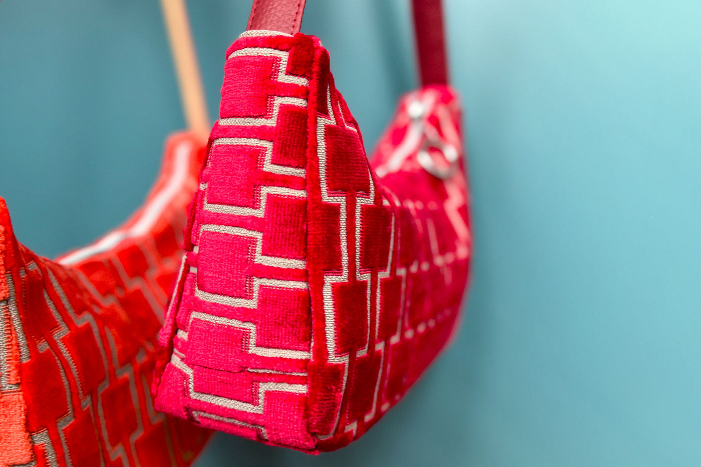 Gesamtansicht: Zwei Schultertaschen im Vintagestil vor blauen Hintergrund. Vordere Tasche ist orange gemustert, die hintere Tasche ist rot gemustert. Beide Taschen wurden von aus upcycled Materialien von Jeff Every Piece A Friend hergestellt.