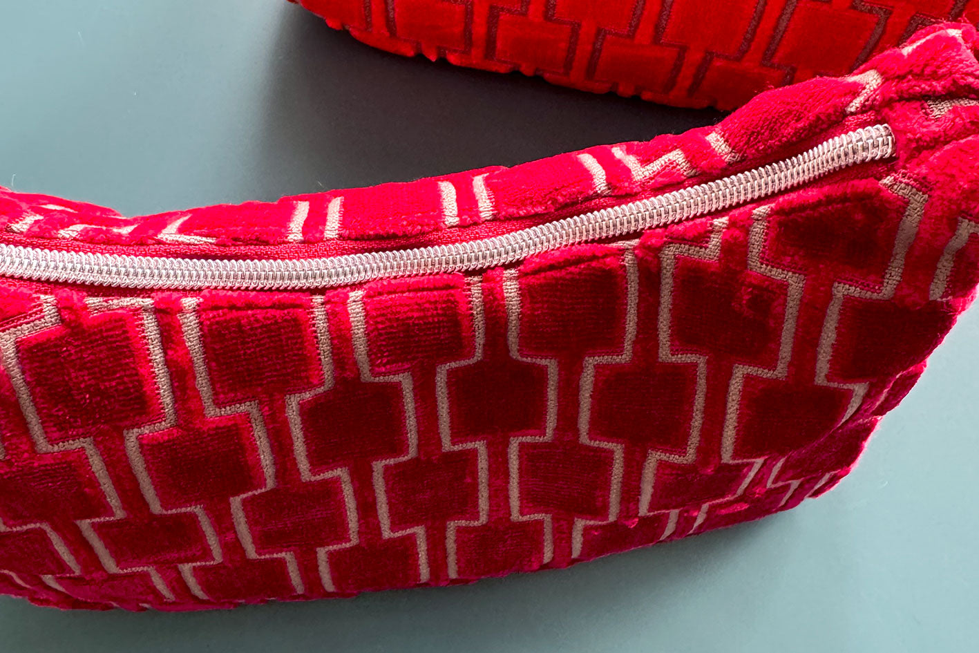 Detailansicht: Zwei Schultertaschen im Vintagestil vor blauen Hintergrund. Vordere Tasche ist rot gemustert, die hintere Tasche ist orange gemustert. Beide Taschen wurden von aus upcycled Materialien von Jeff Every Piece A Friend hergestellt.