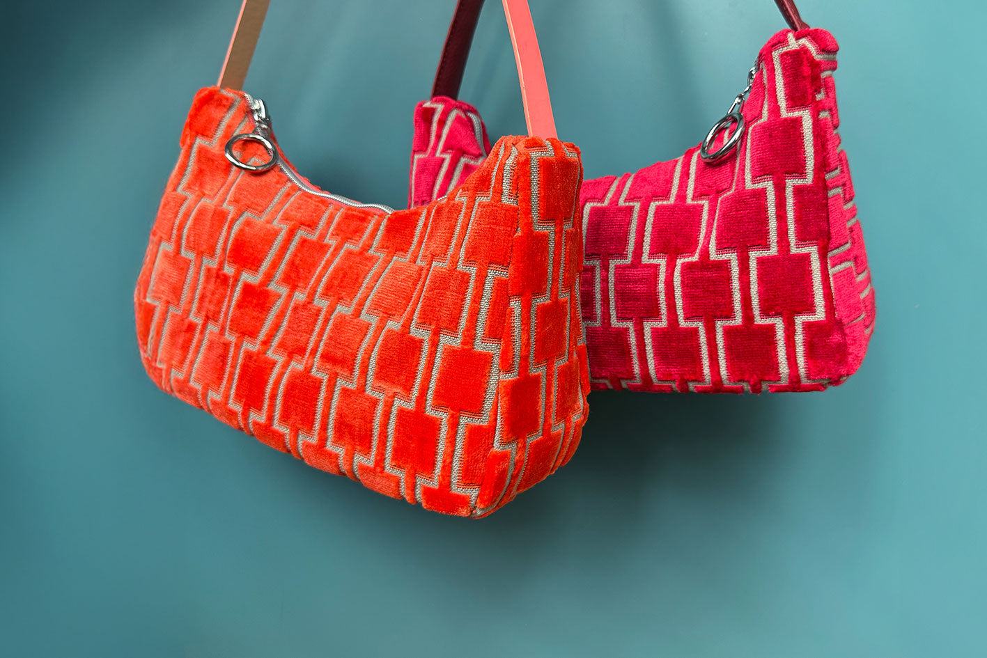 Gesamtansicht: Zwei Schultertaschen im Vintagestil vor blauen Hintergrund. Vordere Tasche ist orange gemustert, die hintere Tasche ist rot gemustert. Beide Taschen wurden von aus upcycled Materialien von Jeff Every Piece A Friend hergestellt.